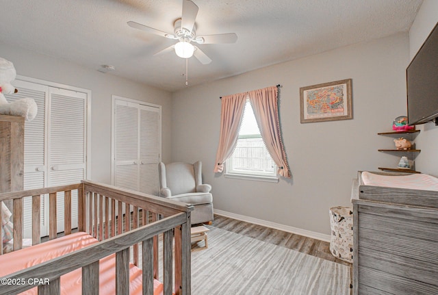 bedroom featuring a textured ceiling, two closets, a nursery area, ceiling fan, and light hardwood / wood-style floors