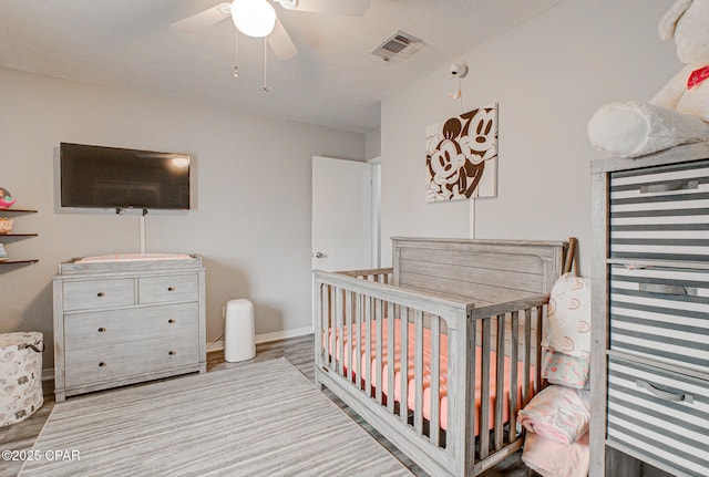 bedroom with light hardwood / wood-style flooring, a crib, and ceiling fan