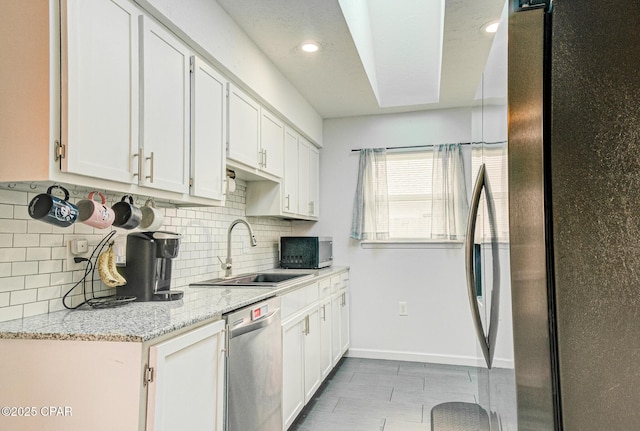 kitchen featuring stainless steel appliances, white cabinetry, sink, and light stone counters