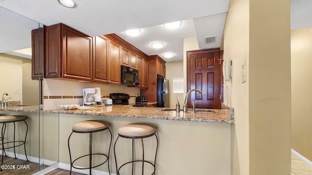 kitchen featuring visible vents, a sink, a peninsula, black appliances, and light stone counters