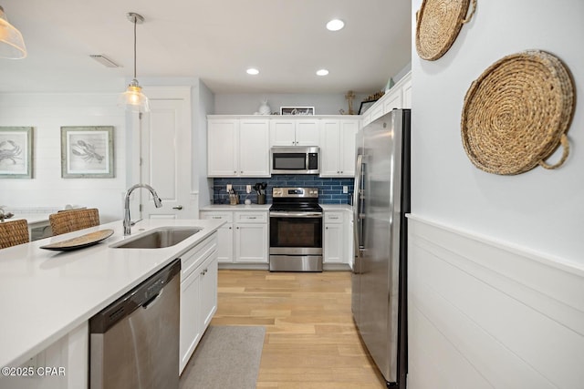 kitchen with sink, decorative light fixtures, light wood-type flooring, appliances with stainless steel finishes, and white cabinets