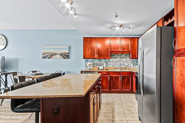 kitchen with a sink, a kitchen breakfast bar, stainless steel fridge with ice dispenser, decorative backsplash, and dark brown cabinets