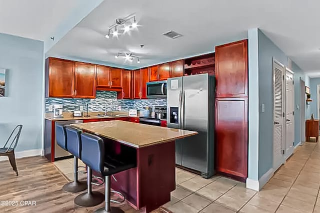 kitchen featuring tasteful backsplash, visible vents, a center island, appliances with stainless steel finishes, and a sink