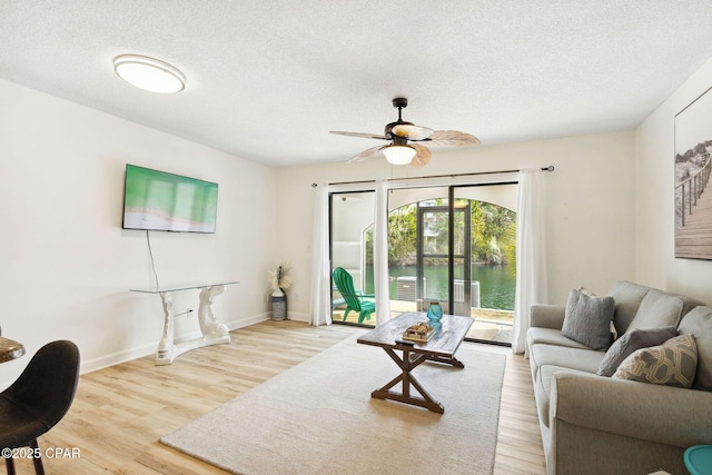 living area with ceiling fan, a textured ceiling, baseboards, and wood finished floors