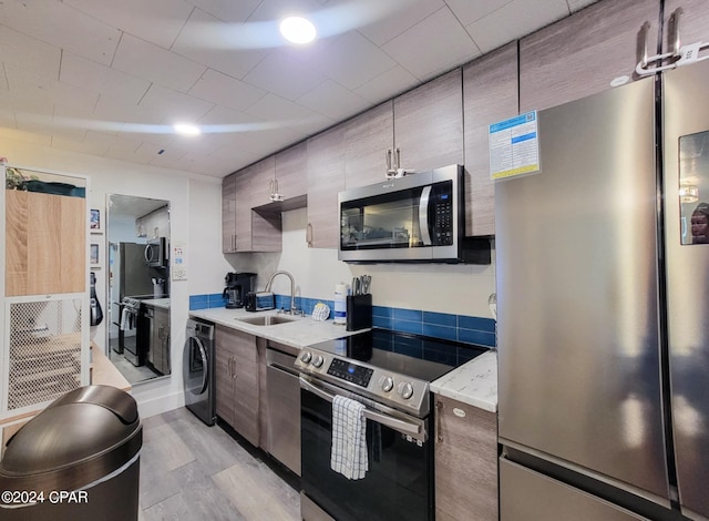 kitchen with a sink, appliances with stainless steel finishes, light wood-type flooring, modern cabinets, and washer / dryer