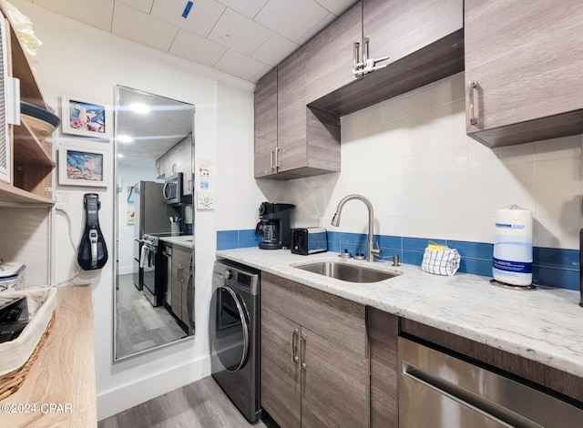 kitchen featuring stainless steel appliances, tasteful backsplash, washer / clothes dryer, light wood-style flooring, and a sink