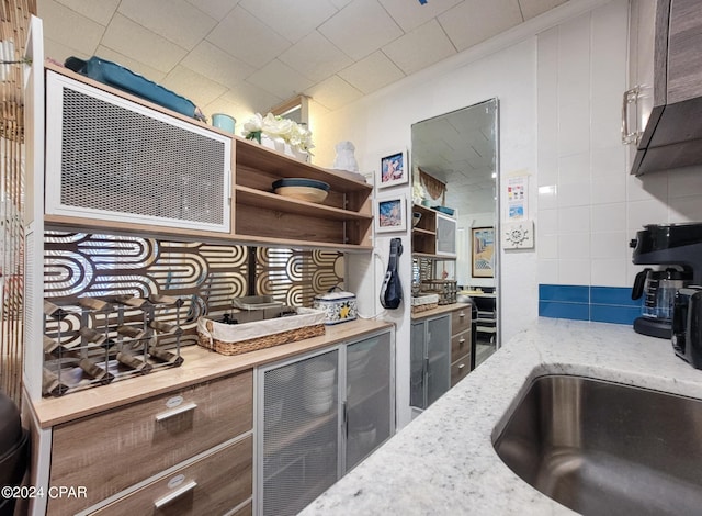 kitchen with tasteful backsplash, light stone counters, open shelves, and a sink