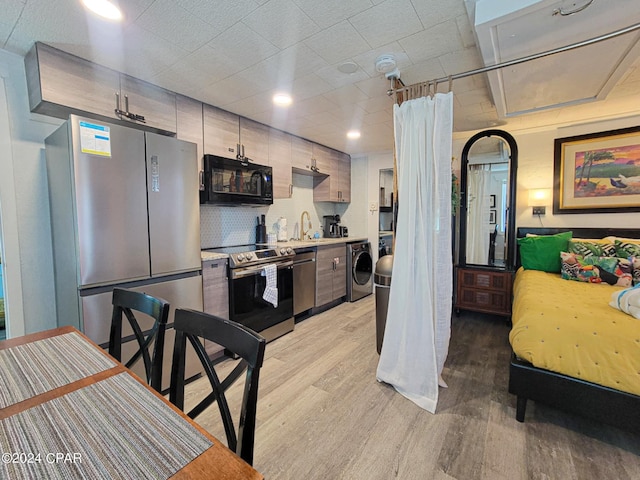 kitchen with light wood-style flooring, stainless steel appliances, a sink, washer and dryer, and light countertops