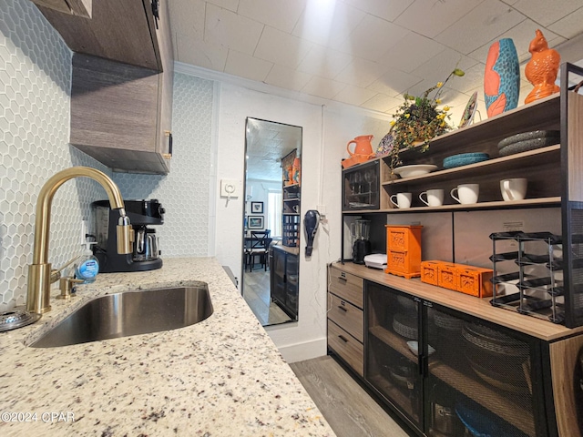 kitchen with wine cooler, a sink, light stone countertops, open shelves, and light wood finished floors