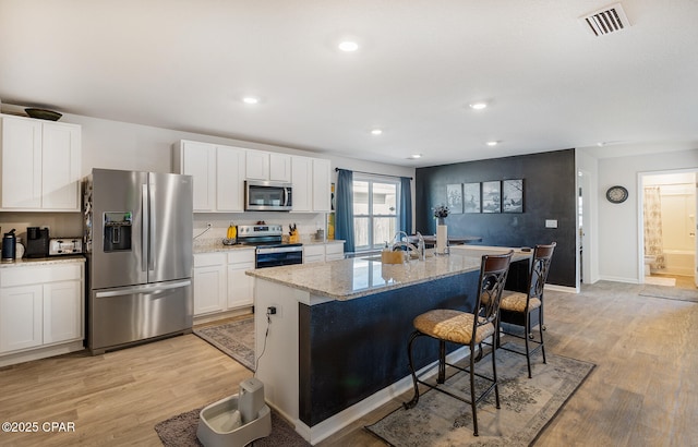 kitchen with light stone counters, white cabinetry, stainless steel appliances, and a center island with sink