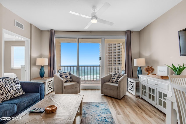 living area with ceiling fan, a wealth of natural light, wood finished floors, and visible vents