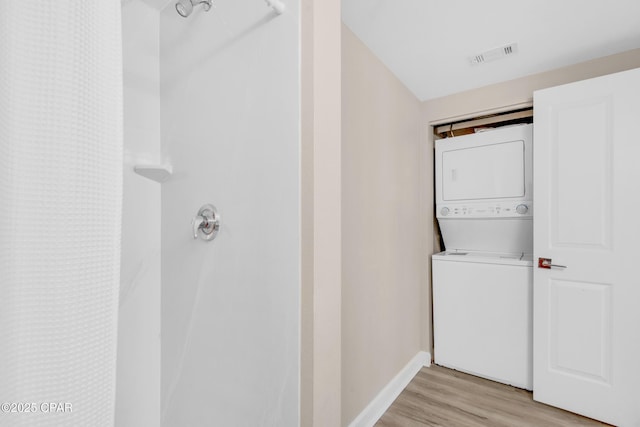 laundry area featuring visible vents, light wood-style flooring, stacked washer / dryer, laundry area, and baseboards