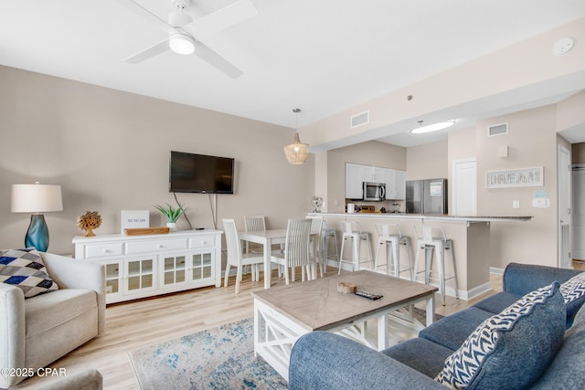 living room featuring visible vents, ceiling fan, light wood-style flooring, and baseboards