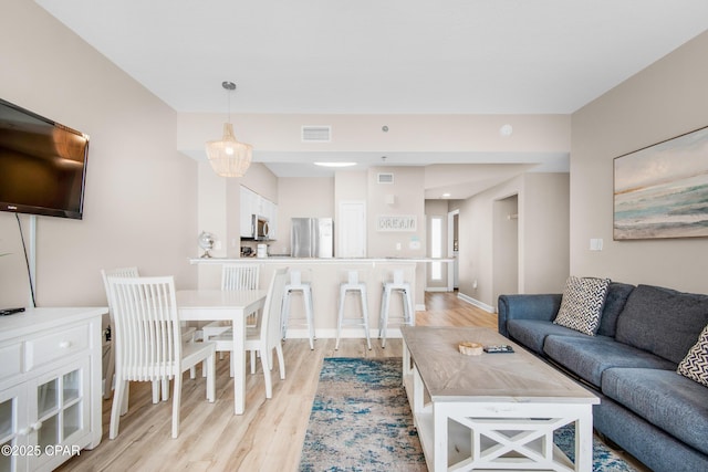 living room featuring light wood-style floors, visible vents, and baseboards