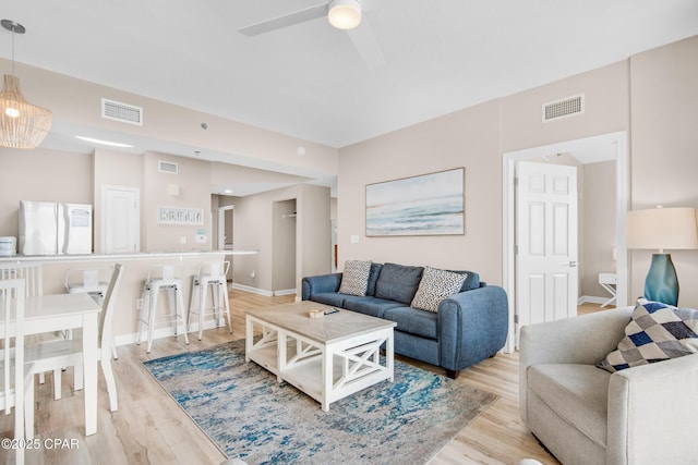 living room with light wood-type flooring, ceiling fan, and visible vents