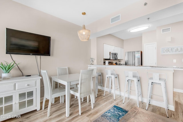 dining room featuring light wood-style flooring, visible vents, and baseboards