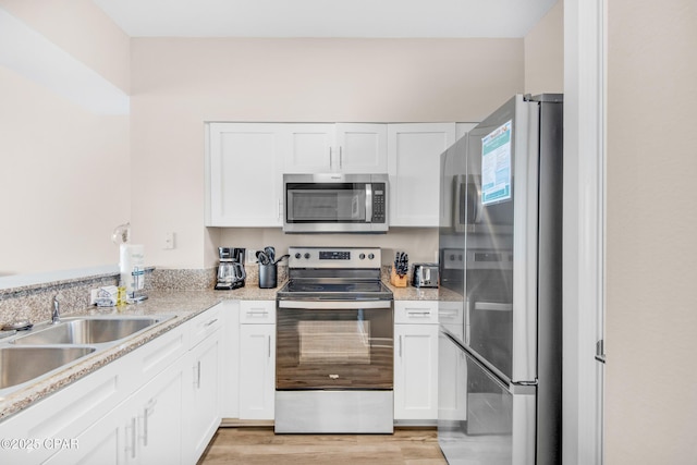 kitchen with light stone counters, stainless steel appliances, a sink, white cabinetry, and light wood finished floors