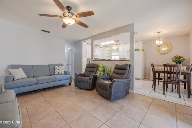 tiled living room with ceiling fan with notable chandelier