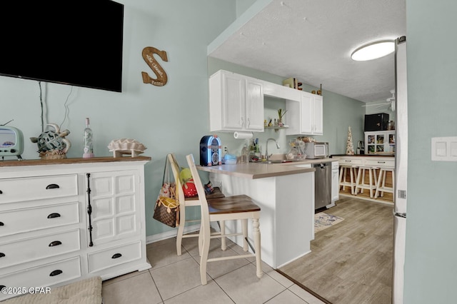 kitchen featuring sink, a breakfast bar area, white cabinets, stainless steel dishwasher, and kitchen peninsula