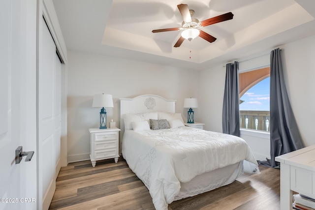 bedroom featuring a closet, dark wood-type flooring, a raised ceiling, and ceiling fan