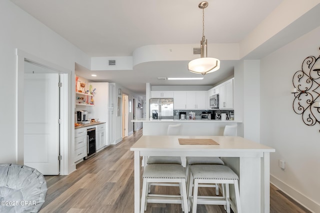 kitchen featuring appliances with stainless steel finishes, pendant lighting, wine cooler, white cabinets, and light wood-type flooring