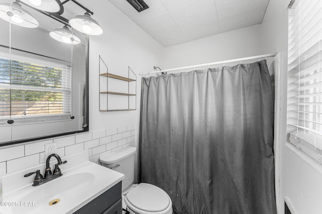 bathroom with vanity, toilet, a shower with shower curtain, and tile walls