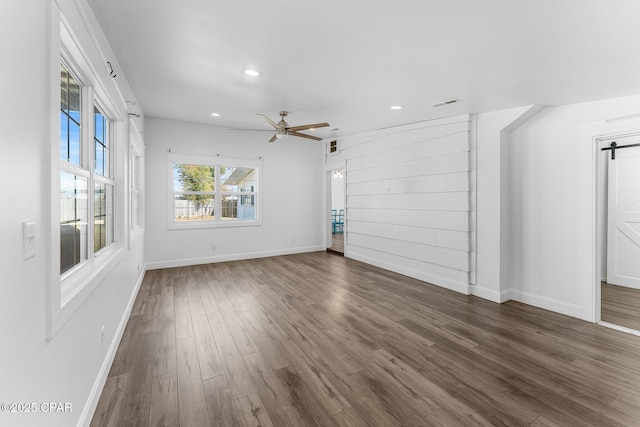 unfurnished living room with ceiling fan, a barn door, and dark hardwood / wood-style flooring