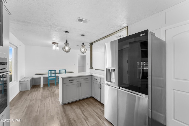 kitchen with gray cabinetry, light hardwood / wood-style flooring, appliances with stainless steel finishes, kitchen peninsula, and pendant lighting