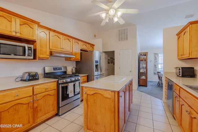 kitchen with vaulted ceiling, light tile patterned floors, a kitchen island, ceiling fan, and stainless steel appliances