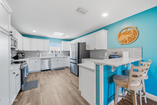 kitchen featuring sink, appliances with stainless steel finishes, white cabinetry, a kitchen breakfast bar, and kitchen peninsula