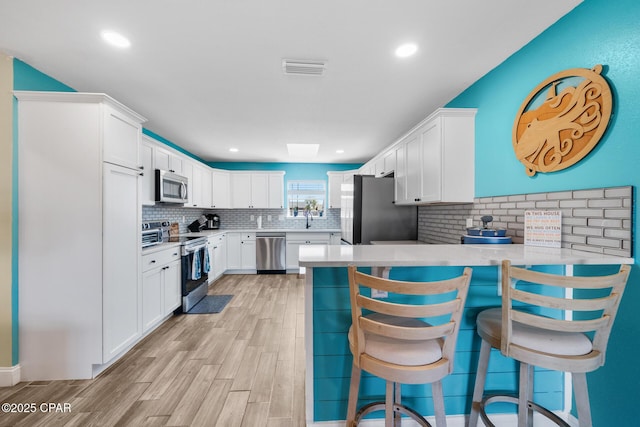 kitchen with stainless steel appliances, a kitchen breakfast bar, kitchen peninsula, and white cabinets