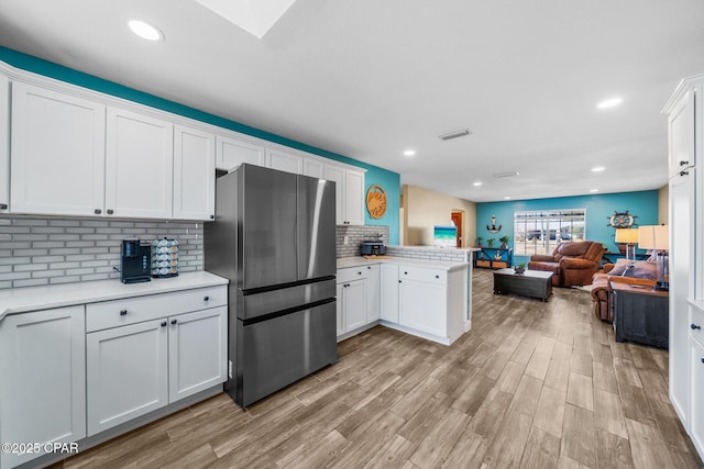 kitchen with stainless steel refrigerator, white cabinetry, decorative backsplash, kitchen peninsula, and light wood-type flooring