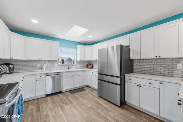 kitchen with sink, appliances with stainless steel finishes, white cabinetry, a skylight, and decorative backsplash