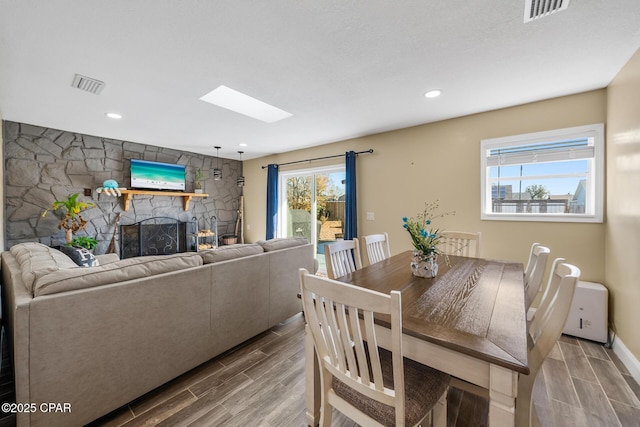 dining room featuring a stone fireplace and a skylight