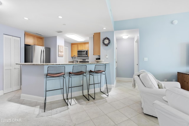 kitchen with appliances with stainless steel finishes, a breakfast bar, sink, light tile patterned floors, and kitchen peninsula