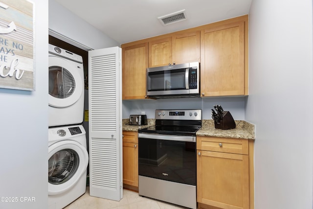 kitchen with light stone countertops, appliances with stainless steel finishes, and stacked washer and clothes dryer