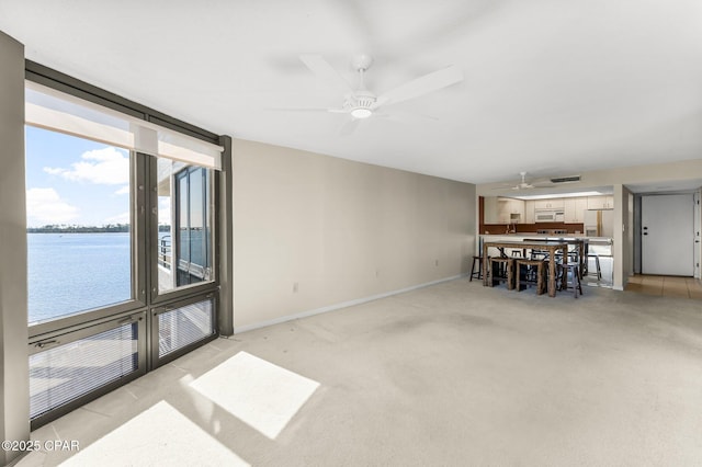 carpeted living area with ceiling fan, a water view, and baseboards