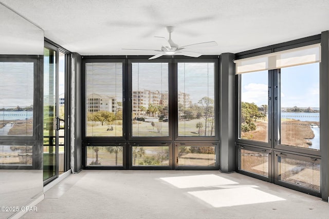 unfurnished sunroom featuring plenty of natural light, ceiling fan, and a water view