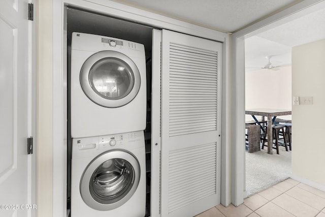 laundry room featuring light tile patterned floors, light colored carpet, a ceiling fan, stacked washer / dryer, and laundry area