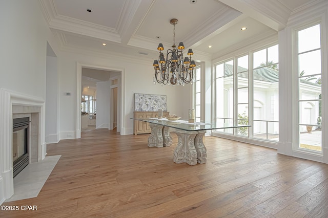 unfurnished dining area with an inviting chandelier, ornamental molding, a tiled fireplace, and light hardwood / wood-style flooring