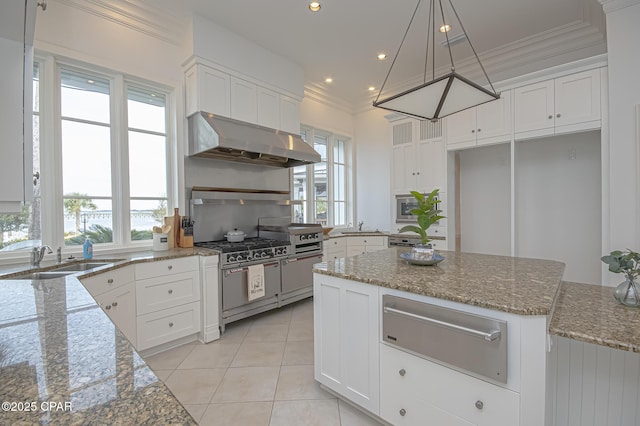 kitchen featuring wall chimney exhaust hood, sink, light stone counters, pendant lighting, and white cabinets