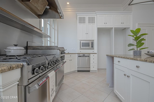 kitchen with appliances with stainless steel finishes, white cabinetry, ornamental molding, light stone counters, and custom range hood