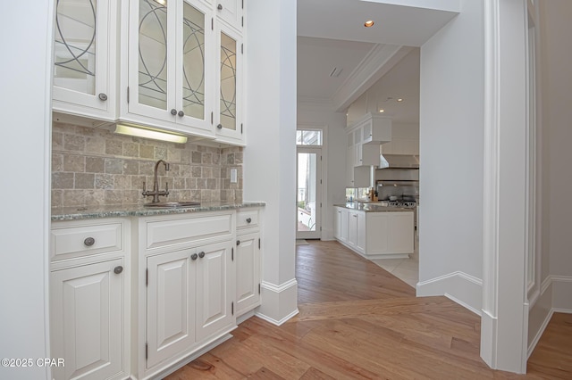 bar featuring sink, white cabinets, ornamental molding, light stone countertops, and light wood-type flooring