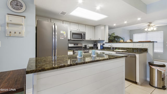 kitchen with appliances with stainless steel finishes, light tile patterned floors, a kitchen island, and white cabinets