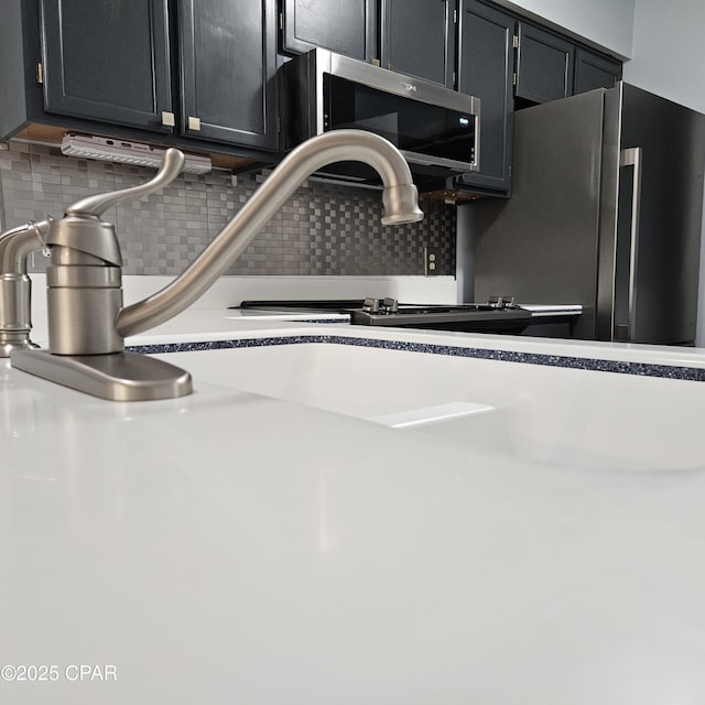 room details featuring stainless steel appliances, backsplash, light countertops, and dark cabinets