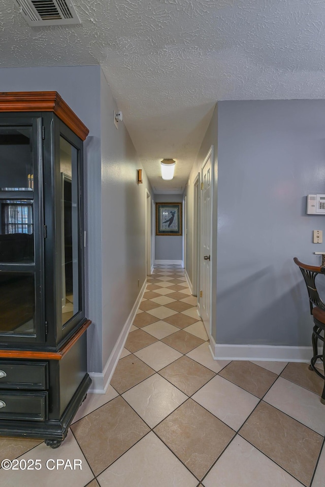 corridor featuring a textured ceiling and light tile patterned floors