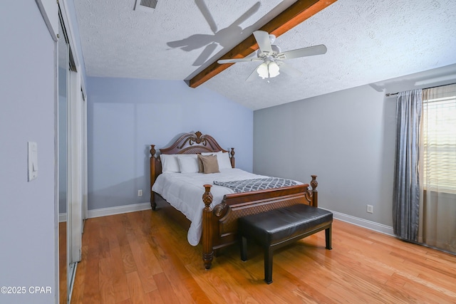 bedroom featuring ceiling fan, hardwood / wood-style floors, a textured ceiling, and vaulted ceiling with beams