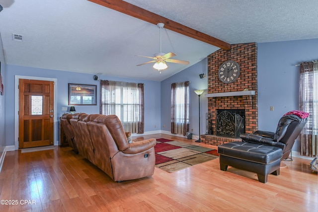 living room with hardwood / wood-style flooring, vaulted ceiling with beams, a textured ceiling, and a fireplace