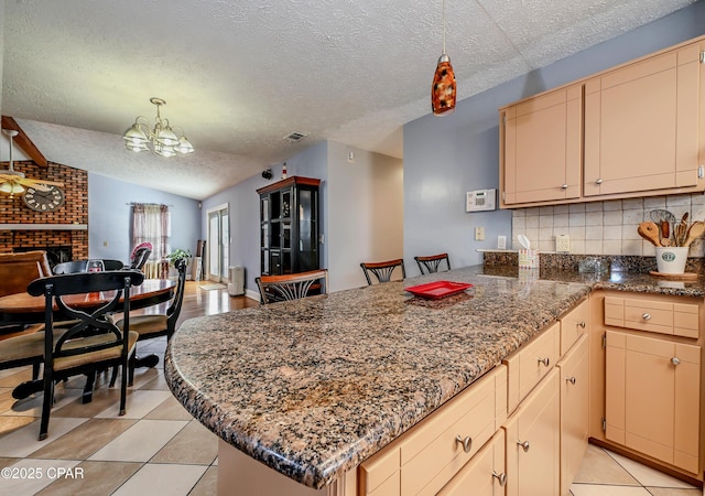 kitchen featuring lofted ceiling, backsplash, a textured ceiling, a brick fireplace, and decorative light fixtures