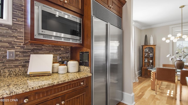 kitchen featuring light stone counters, hanging light fixtures, ornamental molding, and appliances with stainless steel finishes